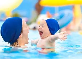 Enfant avec un bonnet s'amusant dans les bras d'une femme dans une piscine 