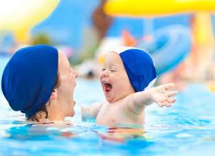 Enfant avec un bonnet s'amusant dans les bras d'une femme dans une piscine 