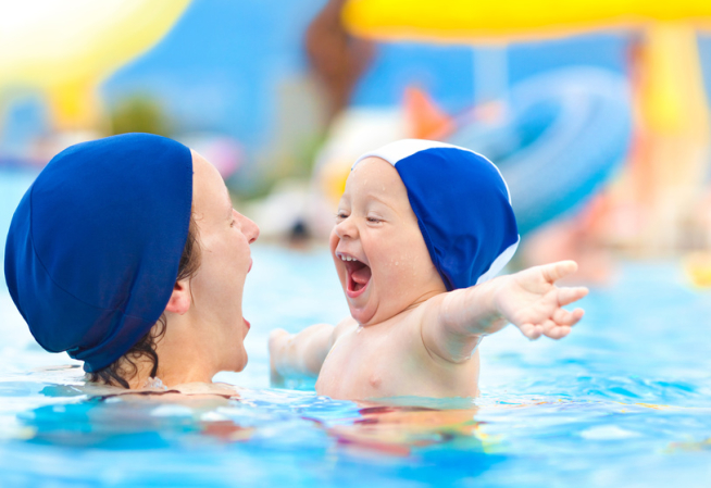 Enfant avec un bonnet s'amusant dans les bras d'une femme dans une piscine 